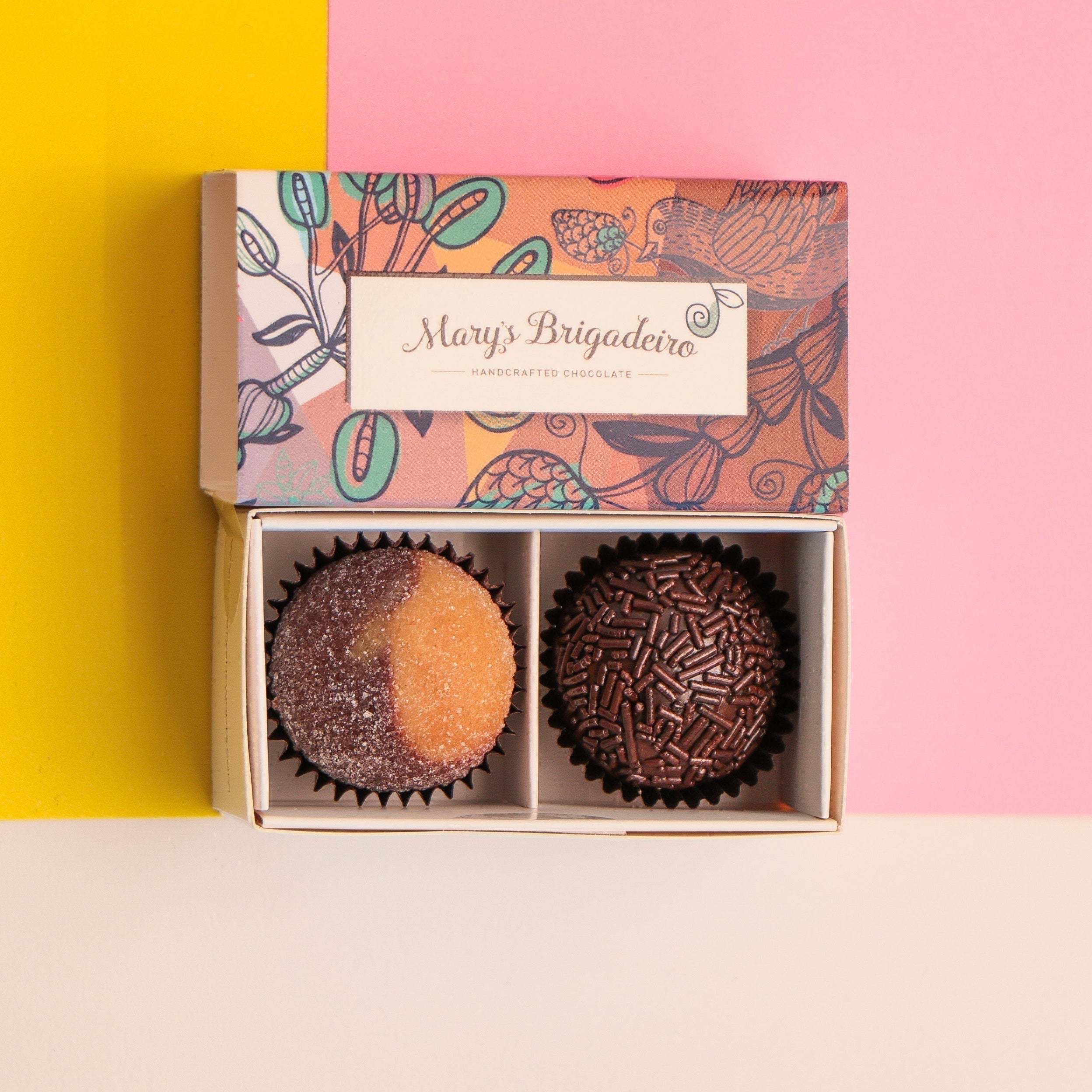 Two chocolates brigadeiros in a gift box on a pink, yellow background.